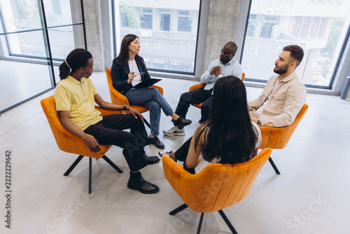 Diverse adults discussing during a group therapy session with a female psychologist leading the meeting