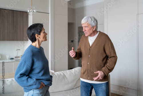 Senior couple in quarrel at home, elderly manipulative husband talking to emotionally distanced wife, problems and ignorance during family conflict, worried man in conversation with frustrated woman.