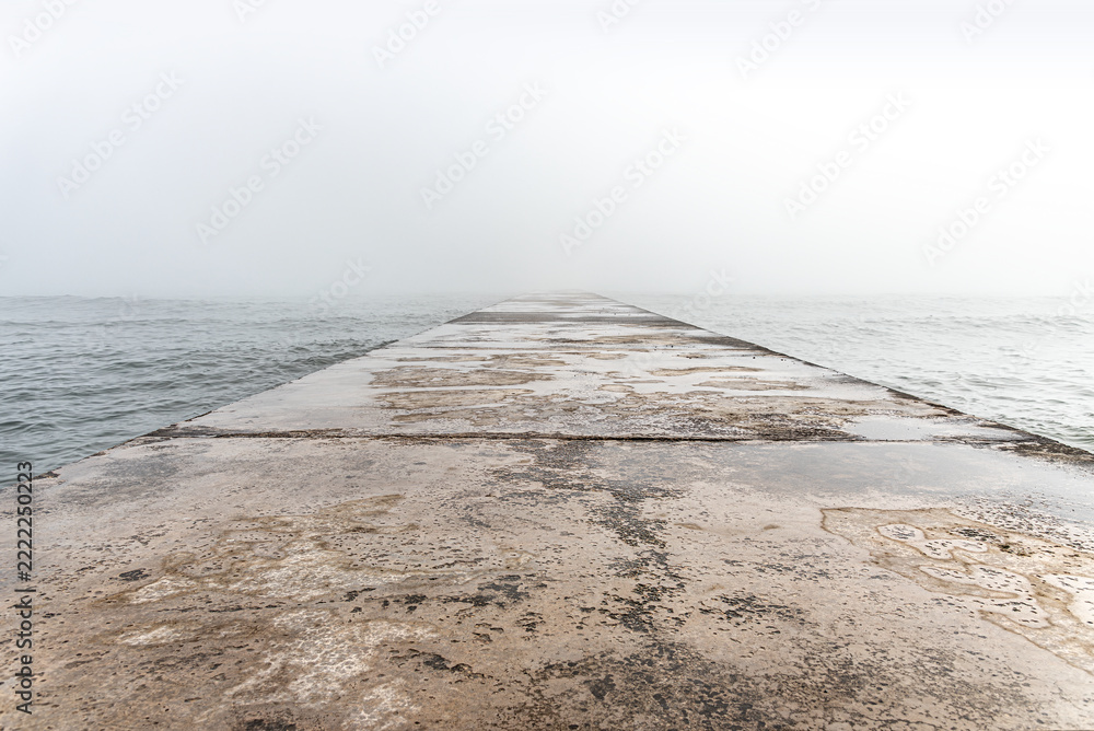 Fototapeta premium A concrete pier extends into calm sea waters on a foggy day.