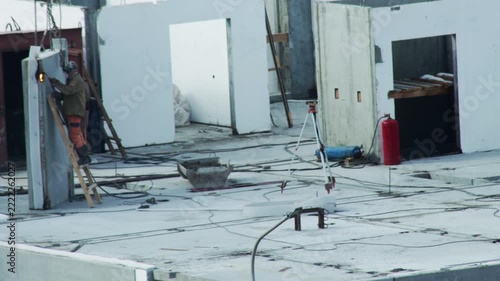 Construction worker welding large concrete panel on building site, sparks flying from metal work, building framework visible