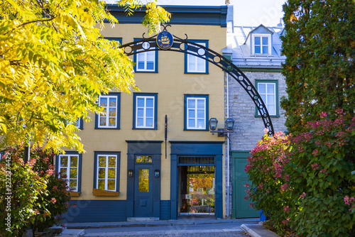 Pretty metal arch with Quebec City medallion at the entrance of lane lined with colourful fall foliage and flowers ending on narrow Ste. Anne street in the old town, Quebec City, Quebec, Canada
