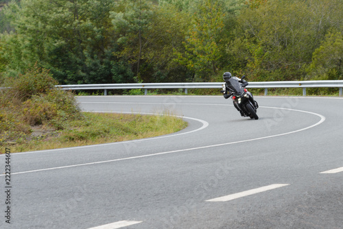 biker on a sport motorcycle rides fast while leaning on a turn on a winding road, motion blur highlighting the dynamic action, close-up