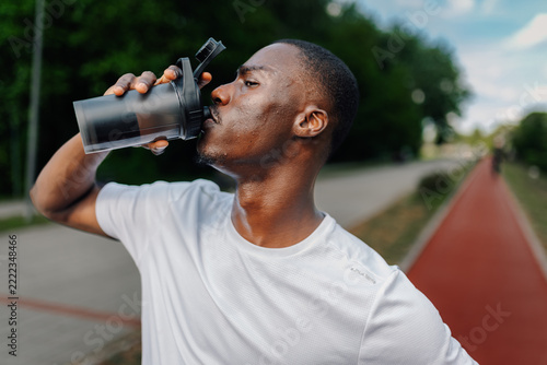 Obraz na plátně Black man hydrating with water bottle after workout