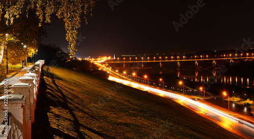 Fotografie Night city panorama with brightly lit bridge over river and long exposure car light trails