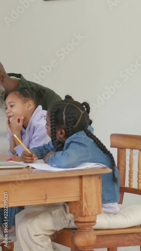 Vertical video: Guiding gramps leaning as notebook opening helping girls in denim writing at home
