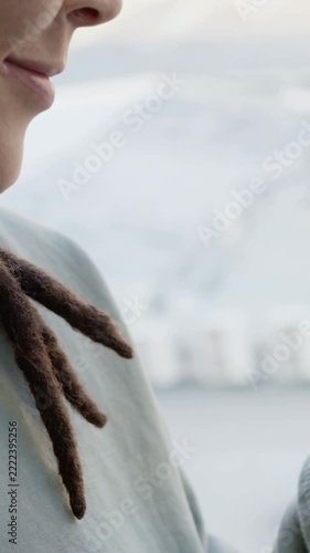 Vertical video: Seeing sea, adult turning and smiling by window with locs, sweatshirt, copy space