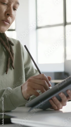 Vertical video: Placing stylus tip, nonbinary person in green sketching on tablet at desk, working