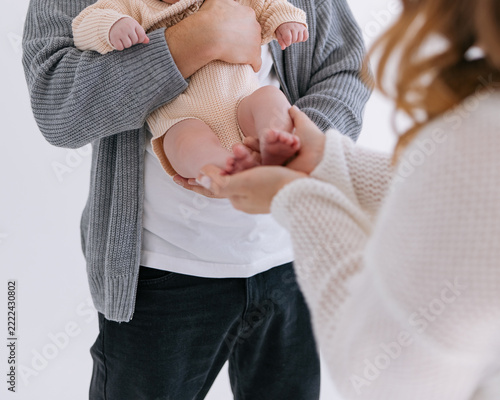 Father holds newborn baby while mother gently touches small feet in cozy room.