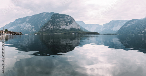 Panoramic view of Lake Hallstatt (Hallstatter See) in Austria, surrounded by majestic Alpine mountains with reflections on calm water and the historic village of Hallstatt on the shore.