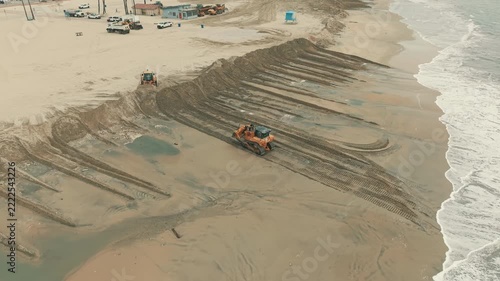 Aerial view of bulldozers pushing sand into protective ridges along Long Beach shore work sites.