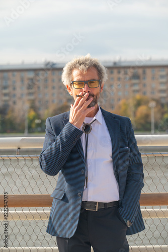 Senior man in eyeglasses smoking cigarette outdoors in city