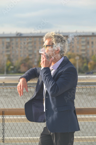 Senior man in eyeglasses smoking cigarette outdoors in city