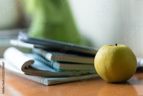 Green apple beside a stack of school notebooks on a wooden desk
