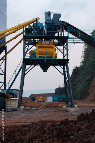 Central mixing station of an industrial concrete batching plant with a yellow twin-shaft mixer at a construction site