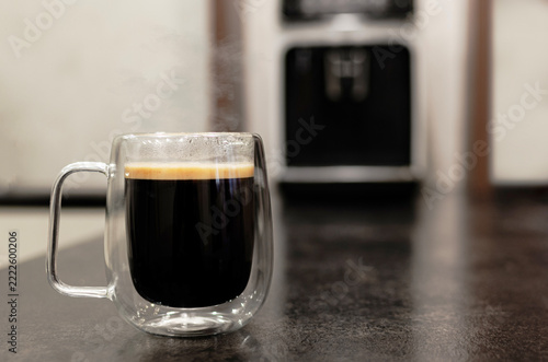 Fresh Hot Espresso in Double Wall Glass Mug with Steam and Coffee Machine Background