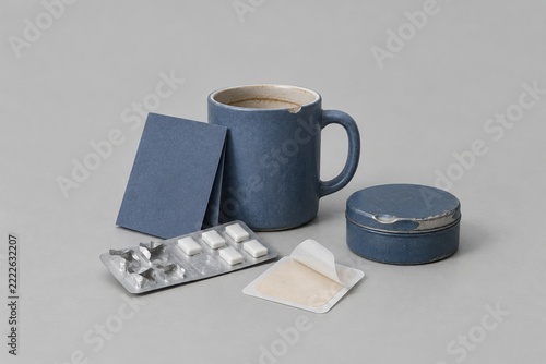 Blue ceramic mug and nicotine replacement therapy kit on a grey surface, featuring a blank leaflet and patch for wellness and recovery copy space