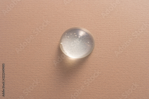 Clear gel drop on textured beige canvas background