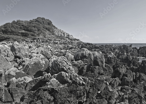 Monochromatic view of a dark and jagged limestone coastline sloping down toward the sea