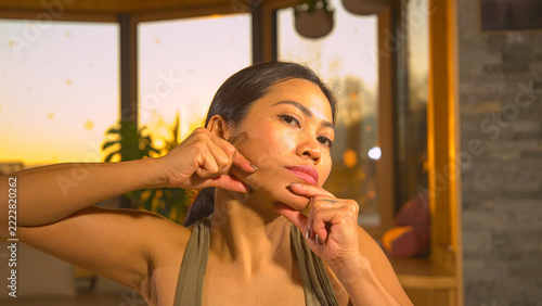 Fotografie CLOSE UP, PORTRAIT: Asian woman practicing facial massage for a defined jawline