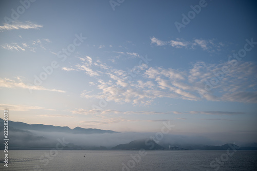 Wide sky with light clouds over morning fog and sea at dawn