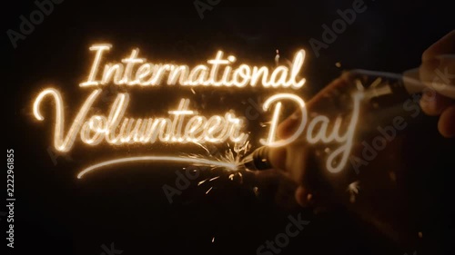 A glowing script text spelling 'International Volunteer Day' with sparks, resembling a lit sparkler, against a dark background, celebrating volunteerism.
