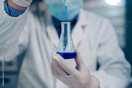 Scientist wearing protective gloves holding two test tubes filled with blue liquid for chemical analysis and scientific research in a laboratory.