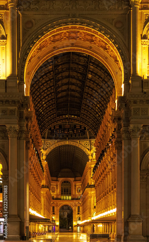 Elegant night view inside Galleria Vittorio Emanuele II in Milan, featuring monumental arches, ornate historic architecture, glass-and-iron vaulted roof and warm golden illumination. Iconic Italian sh