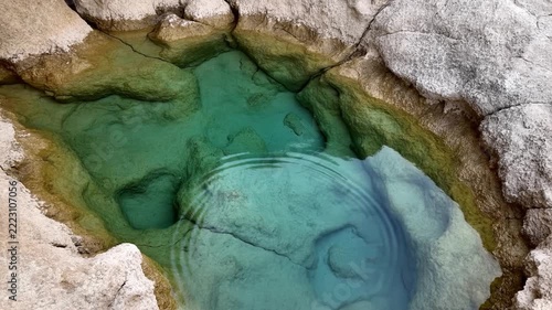 Aerial slow motion pan of turquoise rock pool with rippling water across coastal limestone shoreline