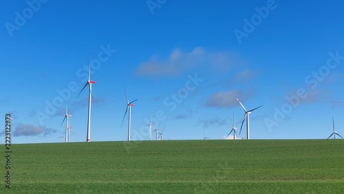 viele Windkraftanlage auf grüner Wiese und hinter dem Horizont bei leicht bewölktem Himmel