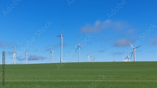 viele Windkraftanlage auf grüner Wiese und hinter dem Horizont bei leicht bewölktem Himmel