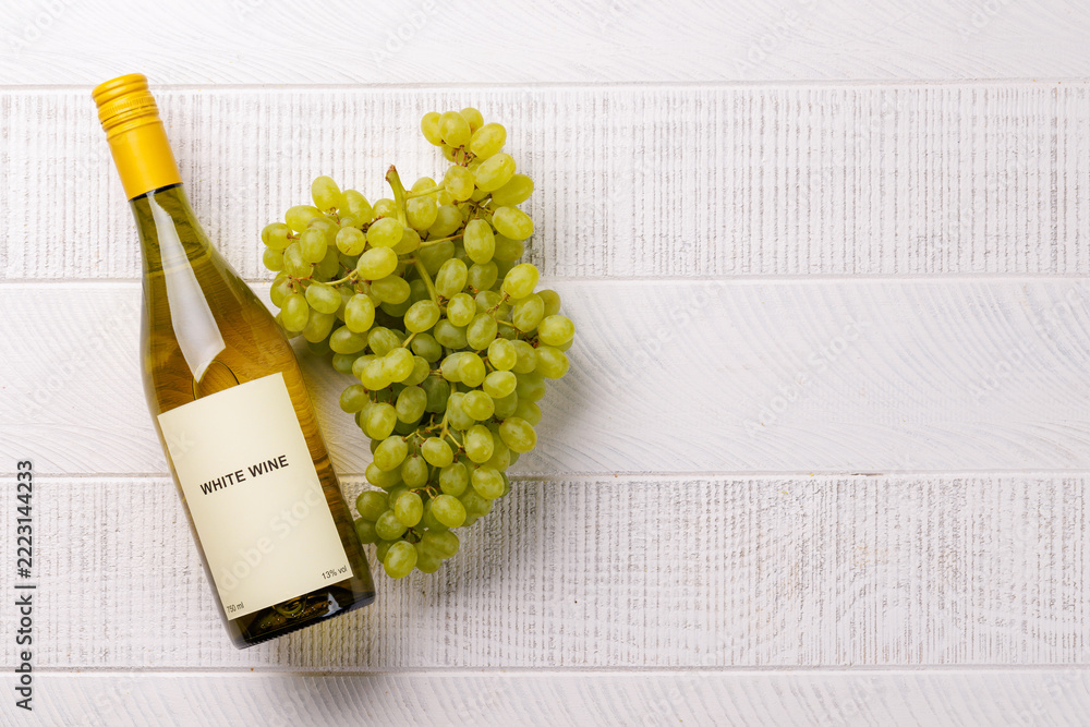 Fototapeta premium White wine bottle and green grapes on white wood