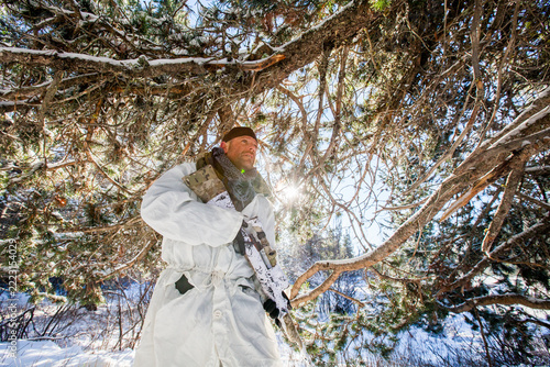 Soldier in winter camo holding rifle in snowy woods