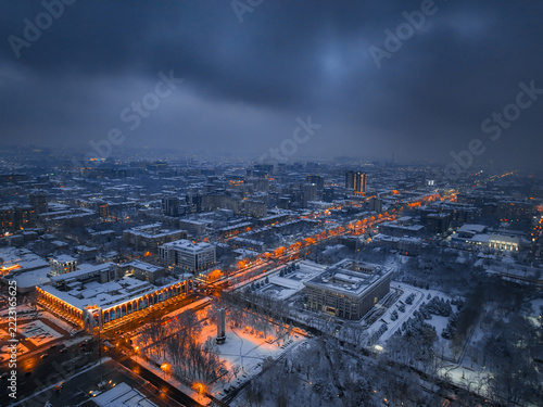 Aerial view of snow covered city buildings and glowing streetlights at dusk