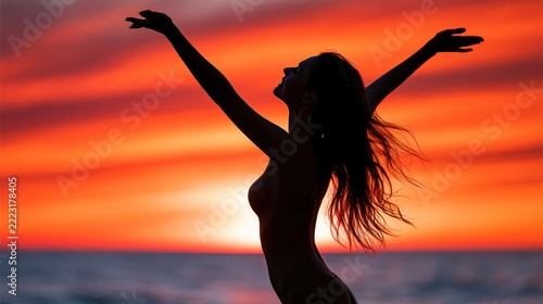 Woman celebrating sunset on beach with arms raised