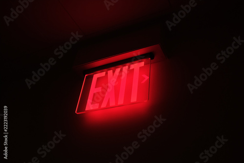Modern Exit sign in dark hallway, made of a transparent frame with red backlighting