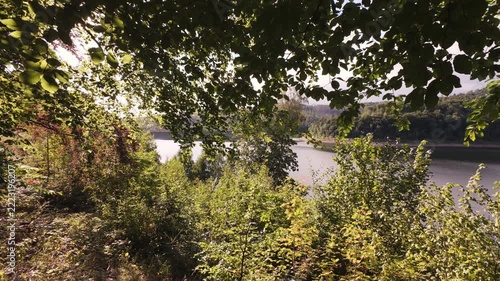 Panoramic reservoir view with calm reflection, wide blue sky with scattered clouds, rolling green hills, dense forest rim, glassy water surface, sunlit foreground, sense of expansive solitude