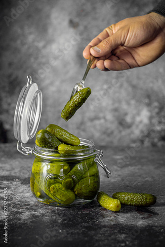 Pickled cucumbers in glass jar with hand and fork