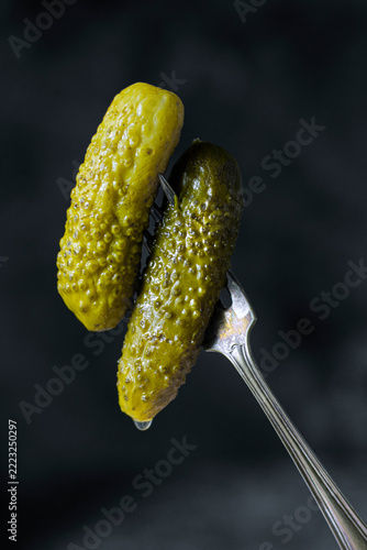 Two pickled cucumbers skewered on a fork with dark studio background