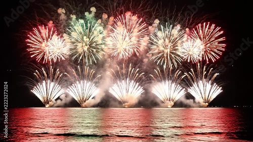 Golden fireworks exploding over dark ocean water at night.