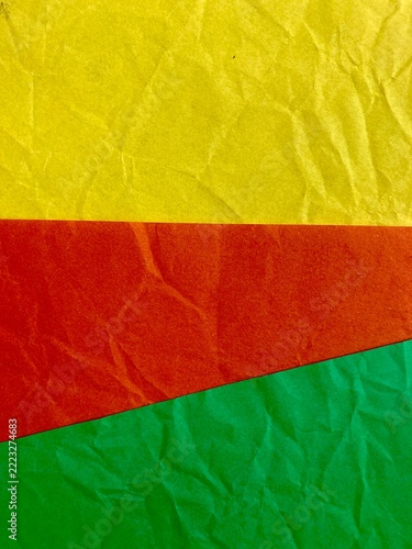 Crumpled paper background features vibrant horizontal bands of yellow, orange, and green creating a textured geometric color block design.