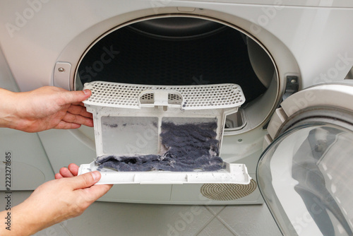 hands removing accumulated lint from a clothes dryer filter during household maintenance