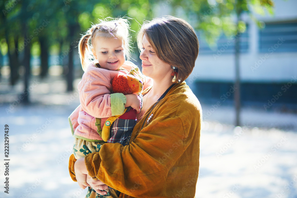Fototapeta premium Smiling mother holding her three year old toddler daughter outdoors in Luxembourg Garden, Paris, on a sunny autumn day