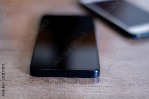 Black smartphone on wooden table with connected mobile technology concept and soft light reflections.