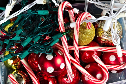 A close up of tangled green and white Christmas lights mixed with glossy ornaments, glittering gold decoration, and red-and-white striped candy canes for the holiday season.