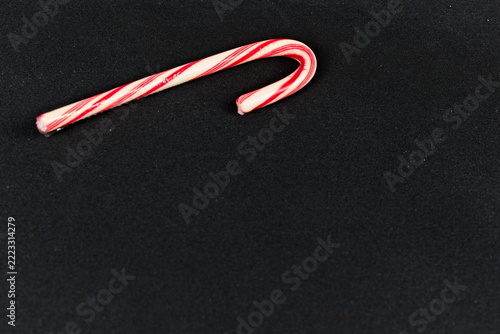 A single red and white striped festive candy cane rests near the top of a dark textured surface, leaving generous open space for seasonal copy.