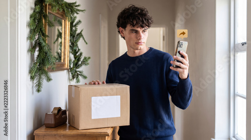 Resourceful sender photographing parcel label with smartphone to ship package from festive hallway