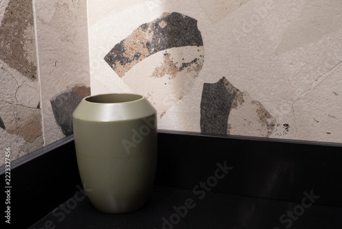 Green ceramic vase on a dark shelf against a beige mosaic pattern wall
