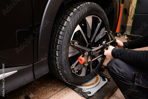 Wheel alignment and alignment on the car service platform. Mechanic performs wheel alignment on a black vehicle in an auto repair shop during daytime