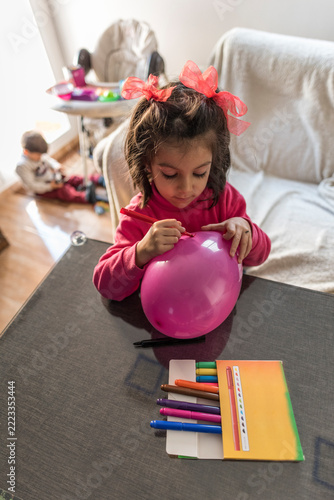 Little girl painting balloon whit her little brother in the background