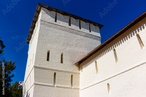 Obraz na plátně Ancient white stone defensive tower of a medieval Russian orthodox monastery against a clear blue sky, imposing fortress architecture with authentic historical brickwork details